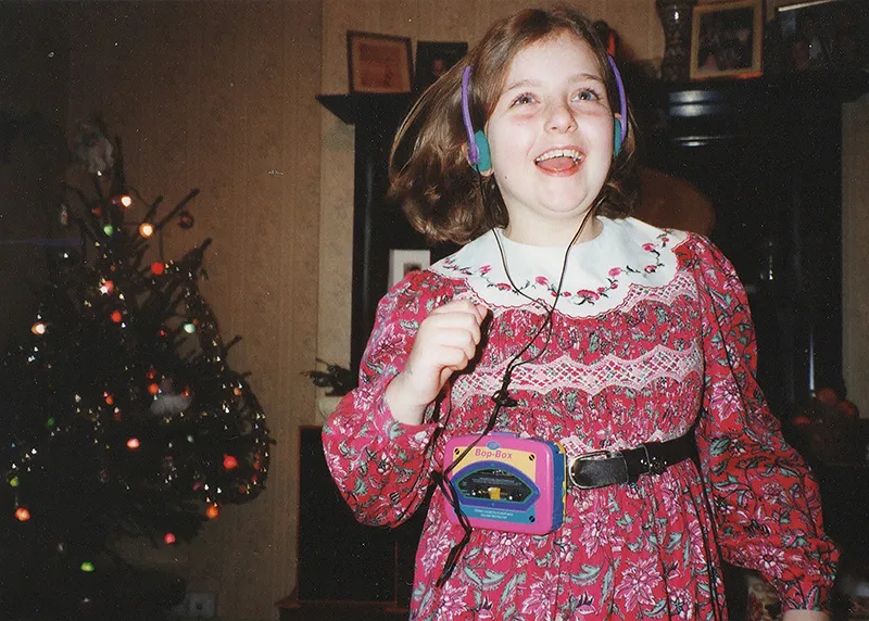 Rosalind as a happy young girl, dancing by the Christmas tree and wearing headphones as she listens to music in her mobile cassette player