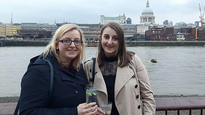 Rosalind and Catherine relax holding drinks, with the River Thames behind them and St Paul's Cathedral in the background