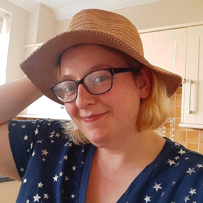 A smiling Ros is wearing a straw hat and a dark blue dress patterned with pale golden stars